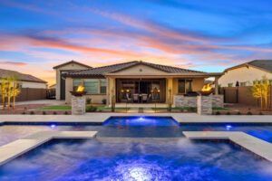 backyard pool and spa in evening with pool lighting, fire bowls and landscape lights.