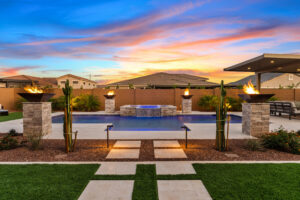 backyard pool and spa in evening with pool lighting, fire bowls and landscape lights.