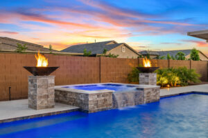 backyard pool and spa in evening with pool lighting, fire bowls and landscape lights.