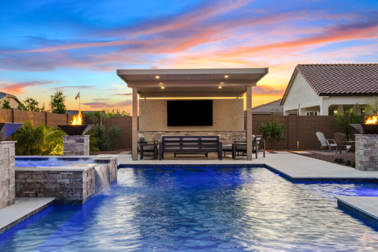 backyard pool and spa in evening with pool lighting, fire bowls and landscape lights.