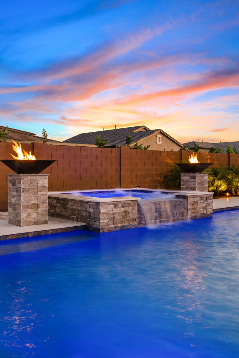 backyard pool and spa in evening with pool lighting, fire bowls and landscape lights.