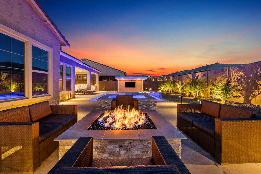 nighttime backyard entertaining with custom built pool, spa, firepit and media wall with outdoor kitchen.