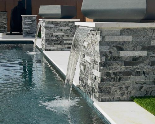 backyard-pool-fountains-jan2025 Swimming pool with waterfall feature.